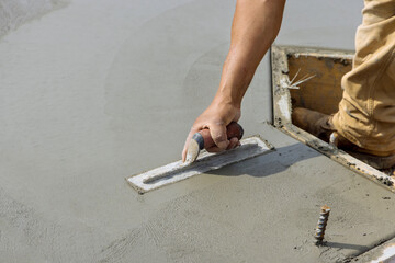 In this a mason worker is holding steel trowel and smoothing plastering concrete onto a cement floor in construction site - obrazy, fototapety, plakaty