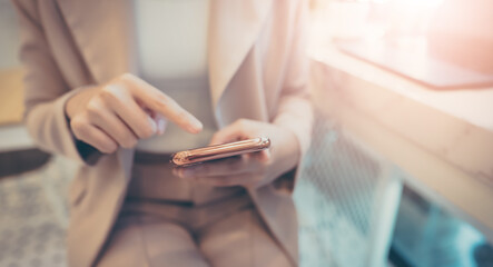 Close up hand of businesswoman using mobile smart phone. She working at cafe workplace