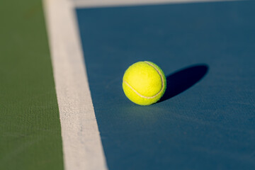 Yellow tennis ball at blue tennis court with white baseline and green out of bounds	