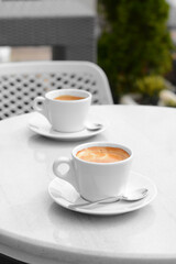 Ceramic cups of aromatic coffee with foam on table in morning