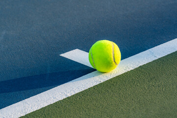 Yellow tennis ball on baseline at center mark on a new blue tennis court with green out of bounds	
