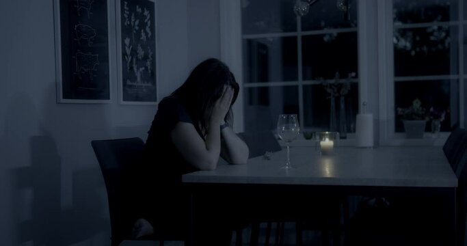 Sad girl cries at dinner table with empty wine glass, pan reveals empty chair