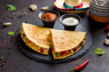 Mexican Quesadilla with chicken, vegetables, cheese and sauces on black stone plate