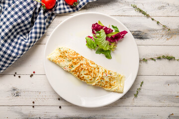 omelette breakfast on a white plate with mix salad on white wooden table top view