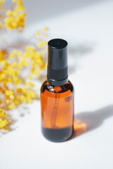 Amber pump bottle with serum, tonic or essential oil with yellow flowers. White background with daylight. Beauty concept for face and body care