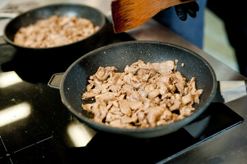 Cook fries meat in a pan with vegetables.