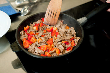 Cook fries meat in a pan with vegetables.