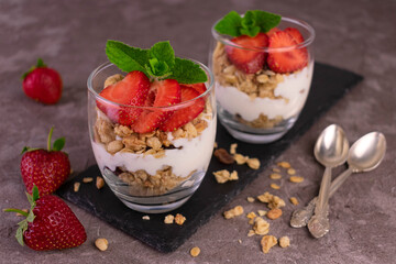 Two strawberry desserts with yogurt and granola on a gray background.
