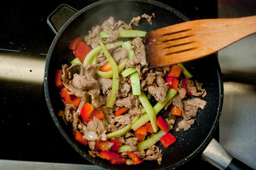 Cook fries meat in a pan with vegetables.