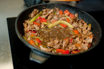 Cook fries meat in a pan with vegetables.