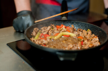 Cook fries meat in a pan with vegetables.