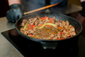 Cook fries meat in a pan with vegetables.