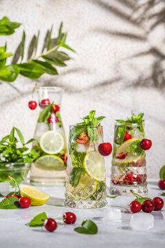 Cherry Mojito cocktail in highball glass or mocktails surrounded by ingredients and bar tools on light gray table surface