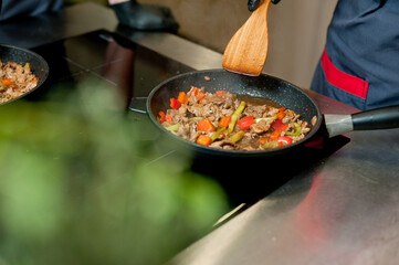 Cook fries meat in a pan with vegetables.