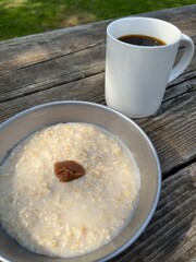 Camping bowl of plain breakfast porridge with pickled plum and white mug of black coffee
