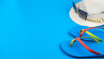 Beach flip-flops, hat and sunglasses on blue backgound. Text space