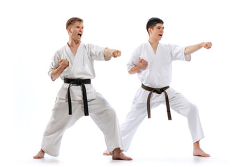 Two athletes, karate-do fighters in doboks practicing karate isolated on white background. Concept...