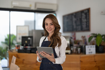 Attractive young beautiful asian barista with apron using digital tablet in coffee shop.