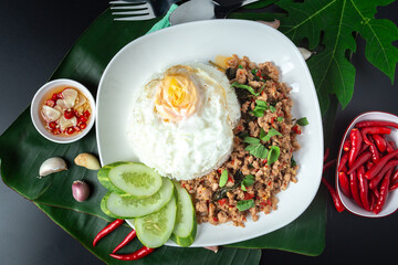 Thai street food, basil fried rice, minced pork, fried egg and sliced cucumber on a black table.
