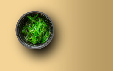 Japanese seaweed salad or wakame seaweed in a cup on a yellow background top view with copy space. © Tanawit
