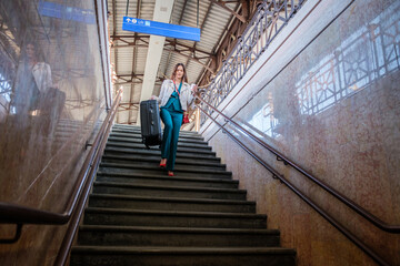 Young woman running down the stairs of the train station with trolley bag - Business woman goes down the steps of the terminal with luggage in her hands