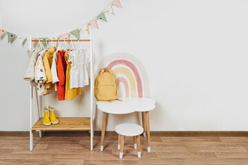 Children's room with Montessori Clothing Rack, white table and rainbow. Dress, jacket and sweaters...