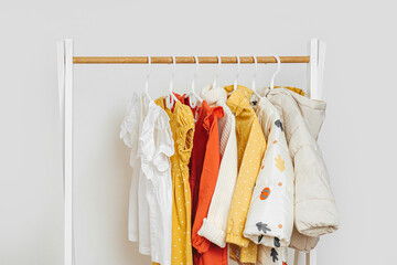 Wooden Clothing Rack with children's autumn outfit. Dress,  jacket and sweaters on hangers in wardrobe close up. Nursery Storage Ideas. Home kids wardrobe.
