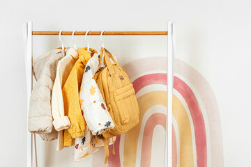 Wooden Clothing Rack with children's autumn outfit. Yellow backpack,  jacket and sweaters on...
