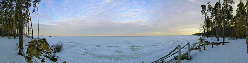 Panoramic photo. Winter river bank. Sunset over the river. 