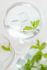Transparent cocktail with ice cubes in a glass decorated with mint leaves close up