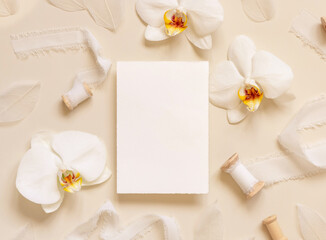 Wedding card near white orchid flowers and silk ribbons on light yellow, mockup