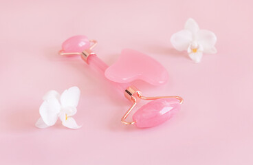 Facial roller and gua sha massager near white orchid flowers on light pink, close up