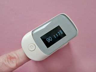 Finger with a pulse oximeter on a pink background close-up. Low saturation on display                        