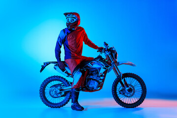 Portrait of young man, biker in professional sports equipment isolated over blue studio background...