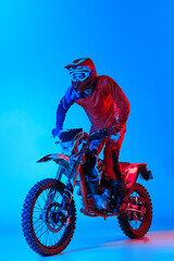 Portrait of young man, biker isolated over blue studio background in neon light. Motocross competition