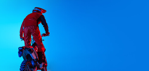 Portrait of young man, biker posing on motorbike isolated over blue studio background in neon...