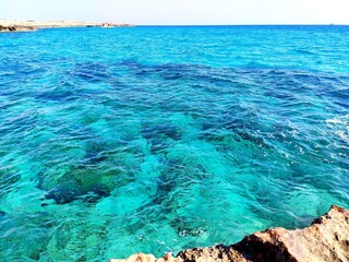 The sea near the rocky coast, shining in the sun, shimmers with many shades of turquoise. Clear sunny day at the sea.