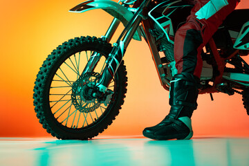 Cropped image of male, biker's leg in boots and tire of motorbike isolated over orange studio...
