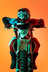 Portrait of young concentrated man, biker developing speed on motorbike isolated over orange studio...