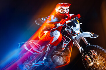 Portrait of young man, biker riding motorbike isolated over black background in neon with mixed...