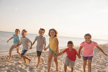 Happy kids running on the beach. Cheerful children having good time at summer holidays. Smiling boys and girls on vacation on seashore.