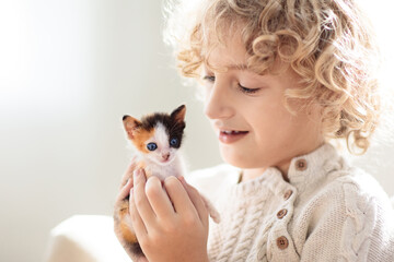 Child playing with kitten. Cat and kid at home.