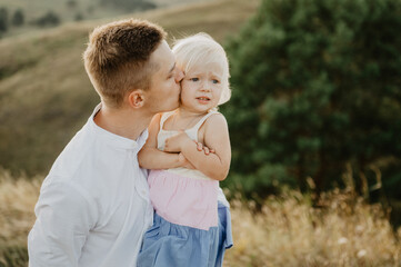 Fototapeta premium Young dad and little daughter hug and kiss on the field at sunset.