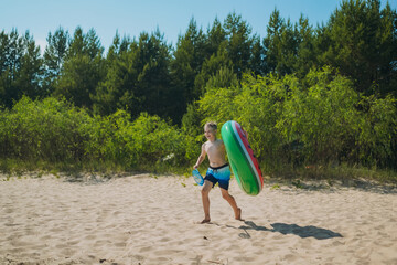 cute caucasian boy carrying rubber ring and butterfly net running into water with laughter. Vacation on sea side. Happy childhood. Image with selective focus.
