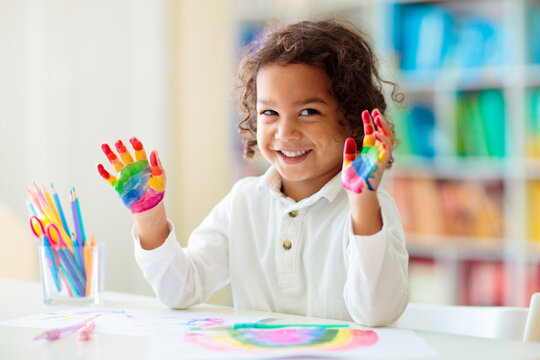 Child drawing rainbow. Paint on hands.