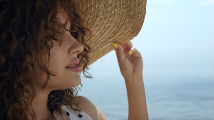 Portrait luxurious woman wearing straw wide brimmed hat on sunny beach. 