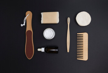 Flat lay top view soap in craft paper, bamboo toothbrush, tooth powder, sponges, face emulsion, pumice stone, bamboo comb on black isolate background. Concept: Zero waste eco friendly bath accessories