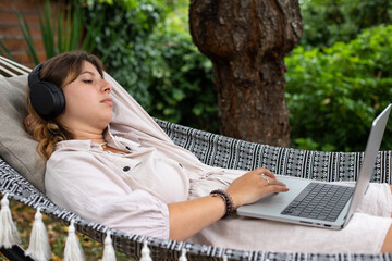Jolie jeune femme allongée dans un hamac dans son jardin. Elle se repose en écoutant de la...