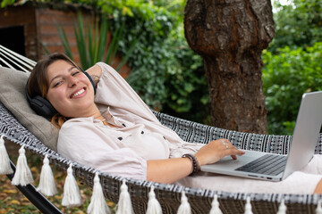 Jolie jeune femme allongée dans un hamac dans son jardin. Elle se repose en écoutant de la...