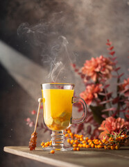 Hot sea buckthorn tea in a glass goblet with fresh, ripe berries and an autumn bouquet of flowers.Close up of hot,healthy drink.